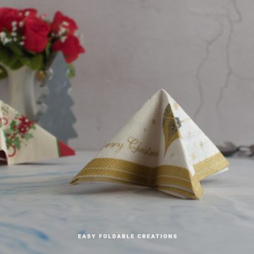 Close up image of a folded white and gold napkin in the shape of a Christmas tree.